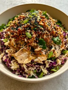 Macro handheld photo of ramen Chinese chicken salad showing the glossy sesame ginger dressing and toasted almond textures.