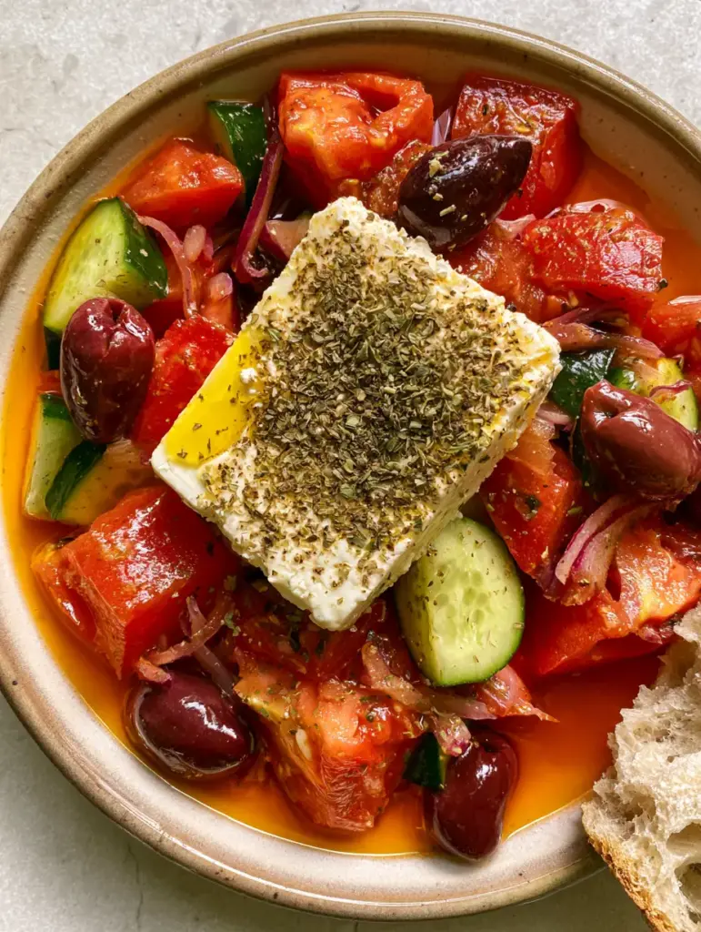 A single thick slab of feta heavily dusted with oregano on top of a Horiatiki salad.