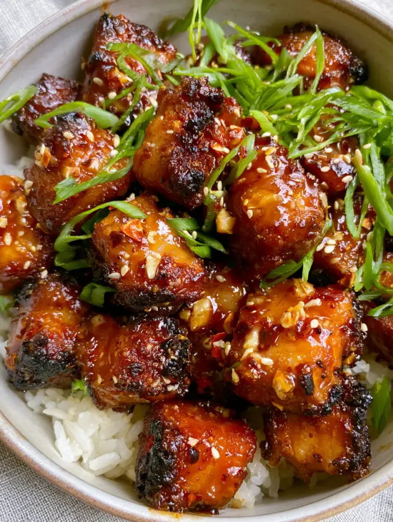Overhead shot of spicy sweet chili garlic pork bites garnished with green scallions and sesame seeds on a bed of rice.