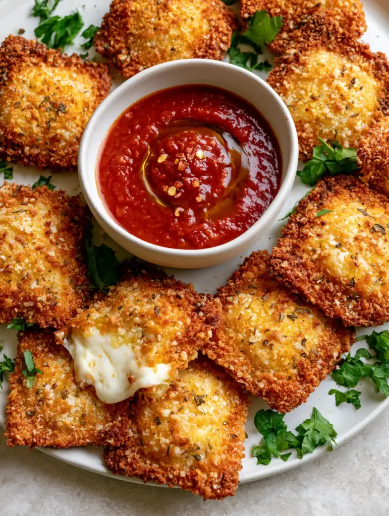 Close-up of Crispy Air Fryer Ravioli being dipped into thick marinara sauce with an olive oil swirl and red pepper flakes.