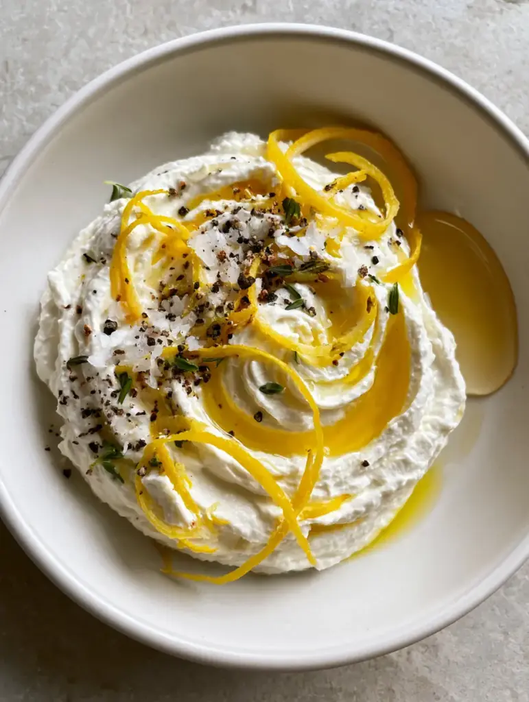 Close-up of Lemon Whipped Ricotta garnished with lemon zest curls, lemon thyme, and cracked black pepper.