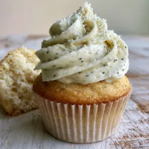 Close-up high-angle shot of a freshly baked Vanilla Cupcake Recipe with iridescent white sugar pearls on a rustic wooden table.