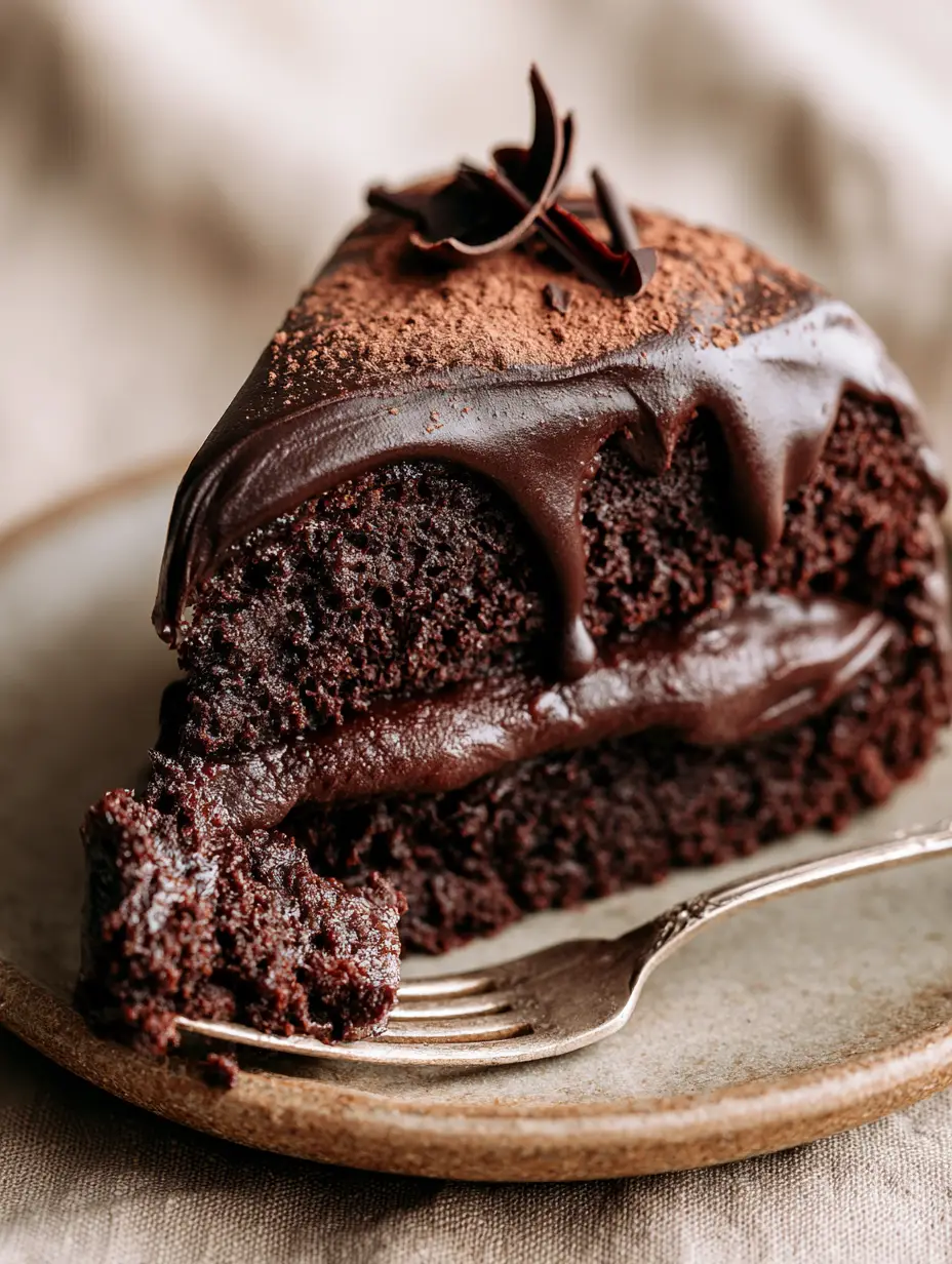 A close-up handheld photo of a moist chocolate cake slice with a clean bite taken out of the front corner. (chocolate cake)