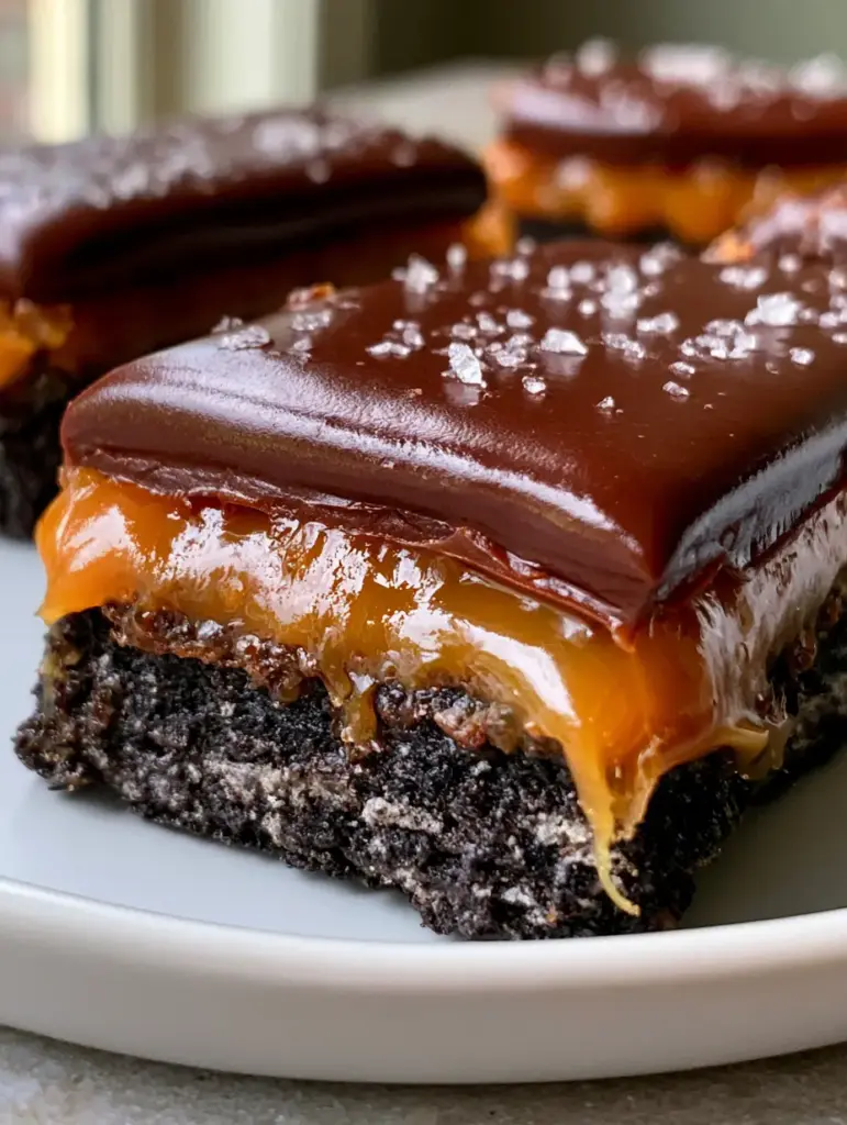 Two Oreo Twix bars stacked on a white plate with flaky sea salt highlighting the dark chocolate top.