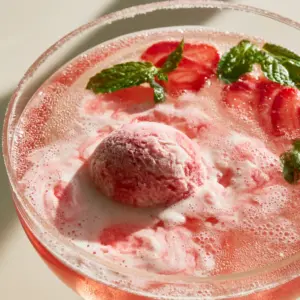 Close-up of creamy raspberry sherbet melting into a sparkling Non-Alcoholic Party Punch with mint garnish.