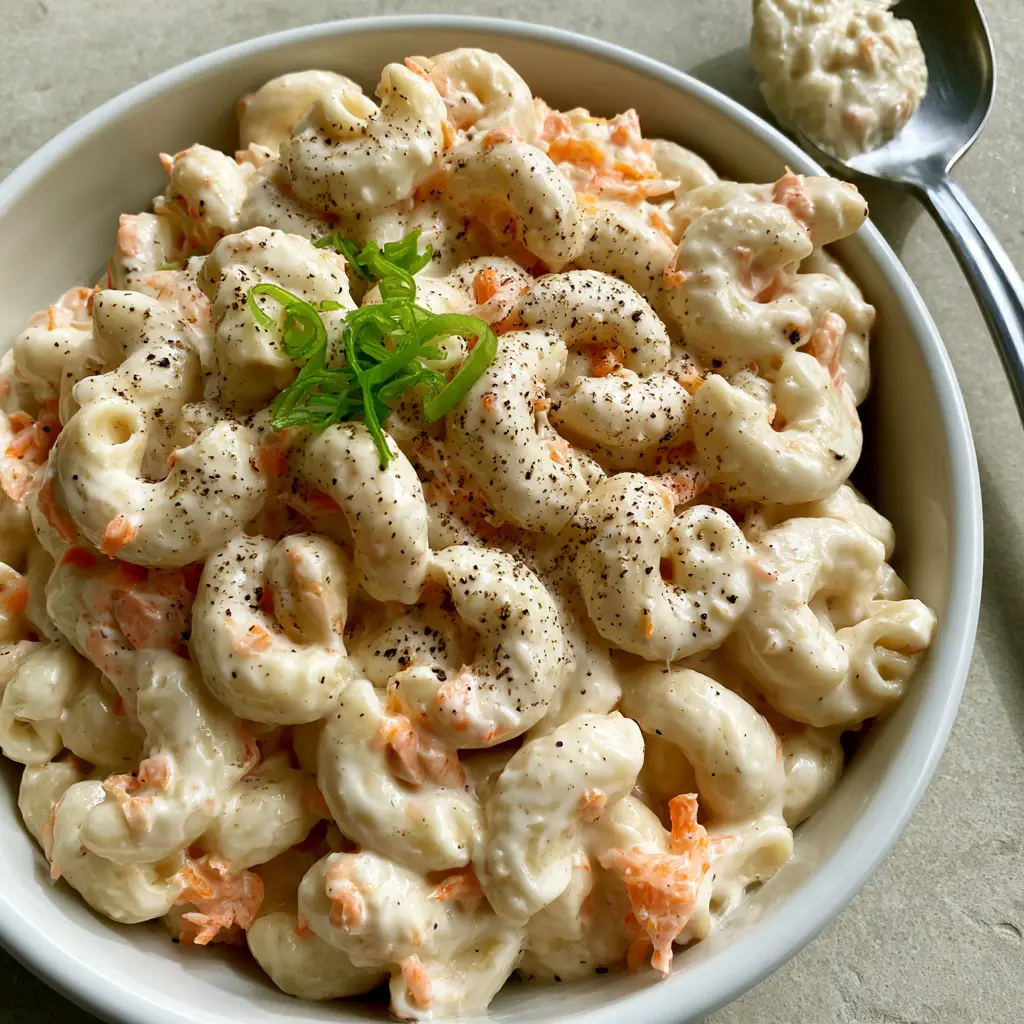 Mo’ Bettahs Macaroni Salad: The Ultimate Creamy Hawaiian Recipe 1 Succulent Hawaiian mac salad in a white bowl with a stainless steel spoon on a gray stone surface.